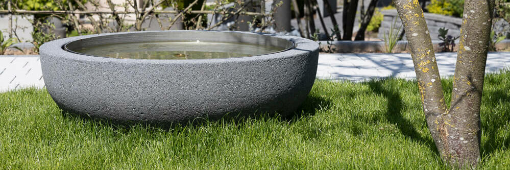 Der Brunnen aus Beton ist ein Highlight im Garten. Mit dem Kontrast des Rasens entsteht eine angenehme Atmosphäre.