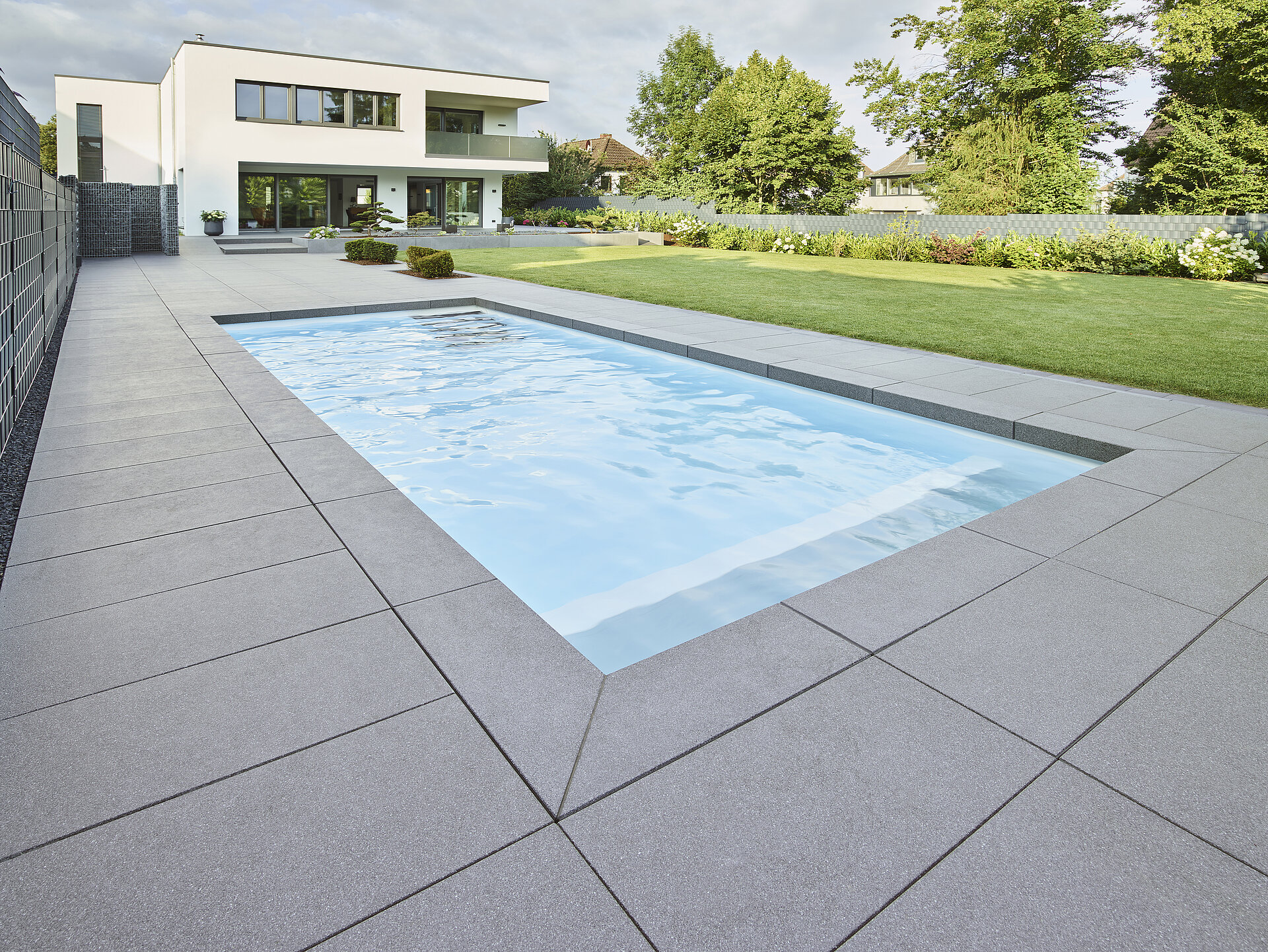 Passend zur modernen Architektur des Hauses wurden um den Pool graue großformatige Terrassenplatten ausgewählt.