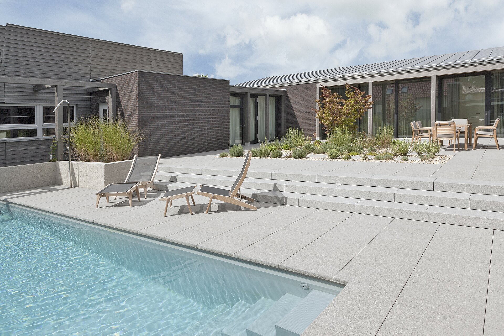 Eine großzügige Terrassengestaltung rund um den Pool. Helle Farben erzeugen ein natürliches Bild.