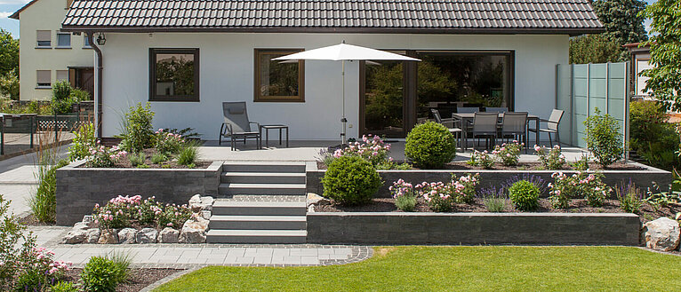 Ansicht hinterm Haus mit Terrasse, Stufen und Mauer.