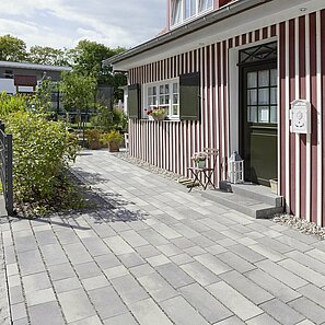 Die grauen Pflastersteine im Hof sind mit großen Fugen verlegt und passen ideal zur rot weißen Hausfassade.